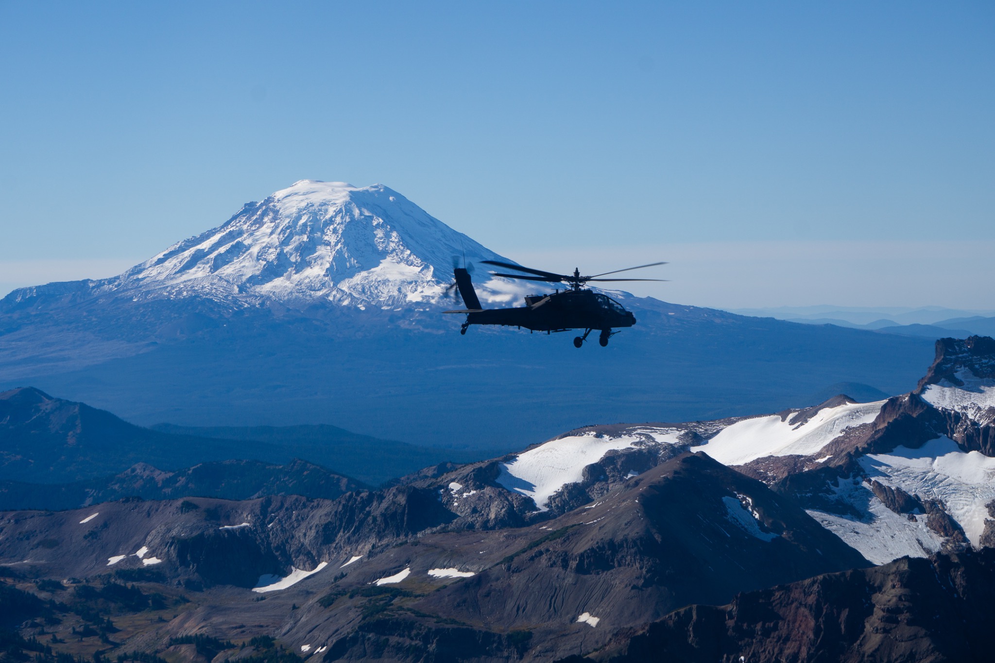 An AH-64 Apache helicopter flying in front of a snow-covered mountain